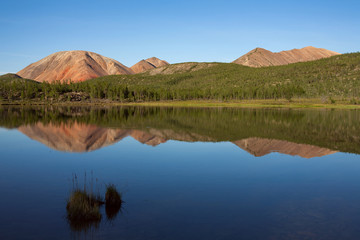 Red Mountain and its reflection in the lake. Oimyakon Highlands. Yakutia. Russia.