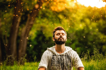 A man sitting on grass in the park and smiling with eyes closed