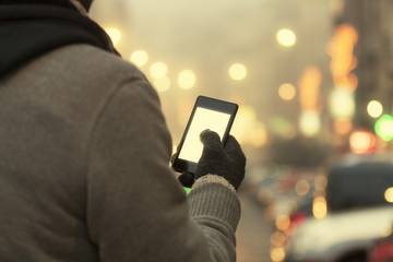 Man using cellphone outdoors with gloves.