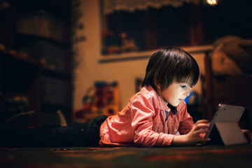 Cute little boy, lying on the floor in kids room, playing on tab © Tomsickova