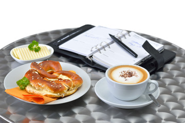 Kaffeepause mit Butterbreze und Cappuccino, ein geöffneter Organizer im Hintergrund