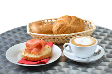 Kleines Frühstück mit Brötchen, Parmaschinken und Cappuccino auf Edelstahl- Bistrotisch