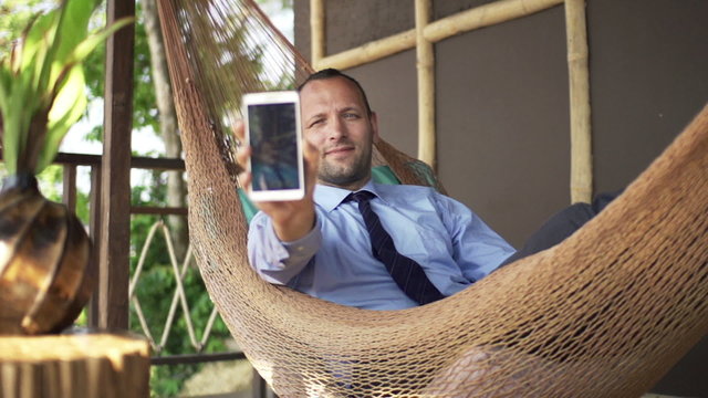 Young businessman taking selfie photo with smartphone on hammock 
