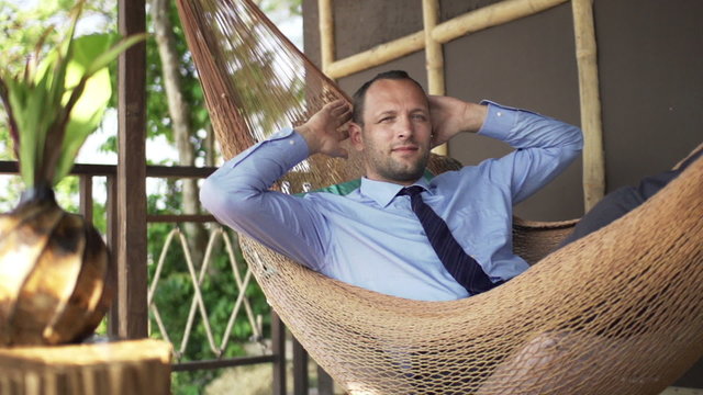 Happy businessman relaxing on hammock on terrace, super slow motion 240fps
