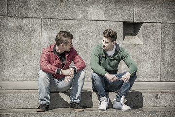 Two young men talking while sitting on curb - Powered by Adobe