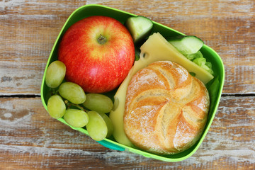 Lunch box containing cheese sandwich, grapes and red apple 
