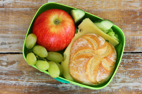 Lunch box containing cheese sandwich, grapes and red apple 
