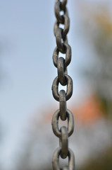 The links of stretched silvery metal chain on a blurred background. Vertical view