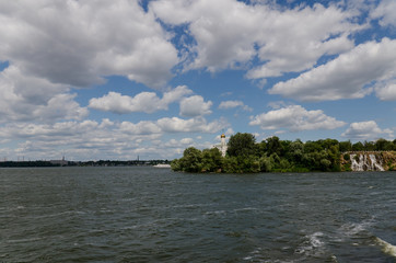 The Orthodox Church in the green river island with a waterfall and a sailing ship on a background of beautiful clouds. A horizontal view. Dnepropetrovsk, Ukraine