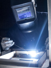 Skilled worker welding metal together in a welding factory - obrazy, fototapety, plakaty