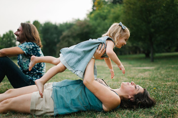 Happy young hipster family having fun while running, bowl,  rising up, piggyback ride their children in park on summer sunset

