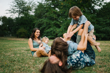 Fototapeta premium Happy young hipster family having fun while running, bowl, rising up, piggyback ride their children in park on summer sunset 