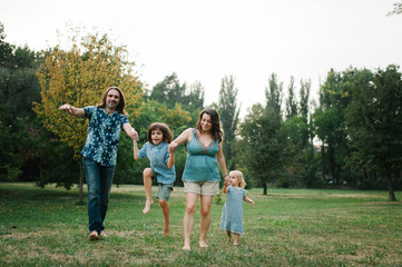 Happy young hipster family having fun while running, bowl,  rising up, piggyback ride their children in park on summer sunset
