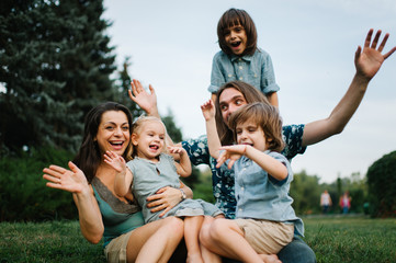 Fototapeta premium Happy young hipster family having fun, bowl, rising up, piggyback ride their children in park on summer sunset 
