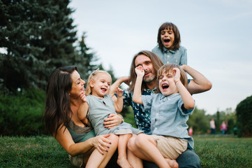 Fototapeta premium Happy young hipster family having fun, bowl, rising up, piggyback ride their children in park on summer sunset 