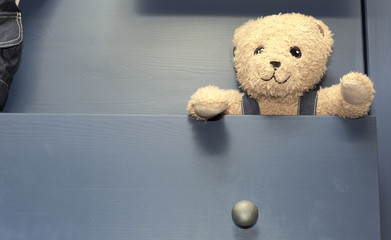 Plush bear sticking out of the dresser. Soft toy bear in the locker.