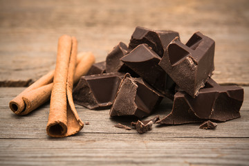 Pieces of chocolate bar with cinnamon on wooden background.