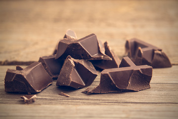 Pieces of chocolate bar on wooden background, toned