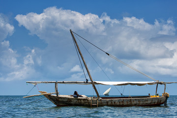 Fototapeta na wymiar Fisherman relaxing on a boat in Zanzibar on a full day with clou