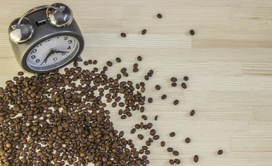 Alarm clock with bells and spilled coffee beans on old wooden table. Top view