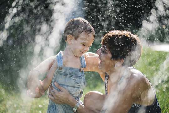Happy little boy and his mother enjoying splashing water in the garden