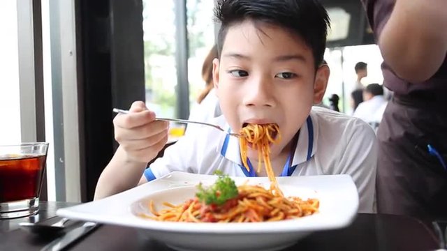 little Asian boy eating spaghetti at restaurant with smile face