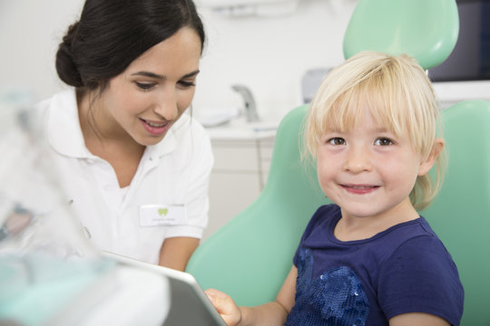 Dentist and smiling girl with digital tablet in dentist's chair