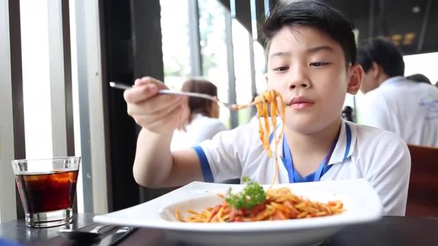 little Asian boy eating spaghetti at restaurant with smile face