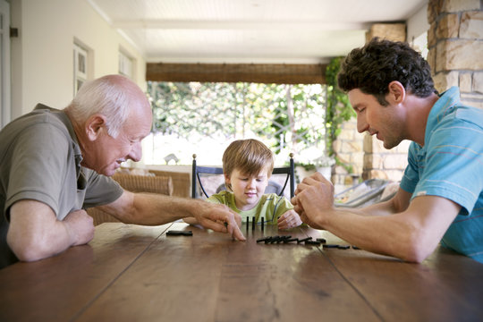 Little boy playing with his father and grandfather domino