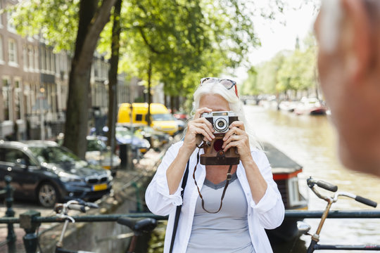 Netherlands, Amsterdam, senior woman taking a picture with analog camera at town canal