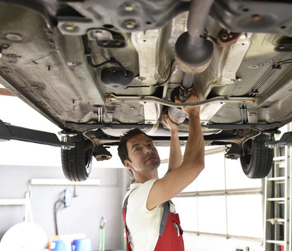 Car mechanic working in repair garage, checking underbody of a car