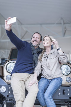 Happy couple at car dealership taking selfie in front of new car