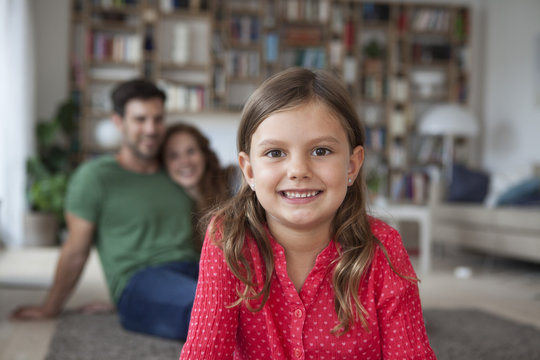 Portrait of smiling little girl and her parents in the background in the living room