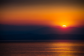 The Rising Sun Over the Sea with Beautiful Vibrant Red Glow. Mountains in Background.