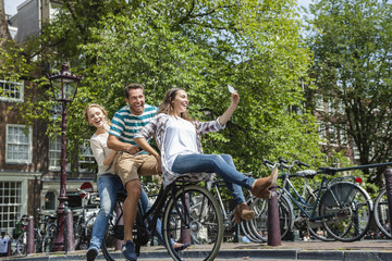 Netherlands, Amsterdam, three playful friends riding on one bicycle in the city