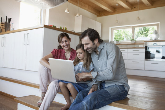 Happy family sitting on kitchen steps, daughter using laptop