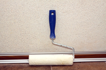 Paint rollers with plastic blue grip, stands in a room at baseboard on the floor near wall, covered...