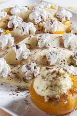 Pancakes stuffed with vanilla cream and peach, decorated with whipped cream and grated chocolate, served on a white plate.