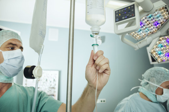 Operating Room Nurse Checking The Drip Of An IV Bag During Surgery