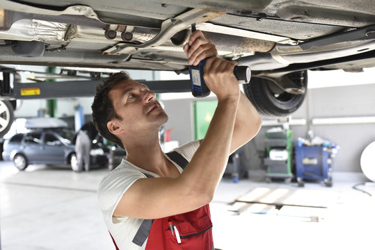 Car mechanic working in repair garage, repairing underbody