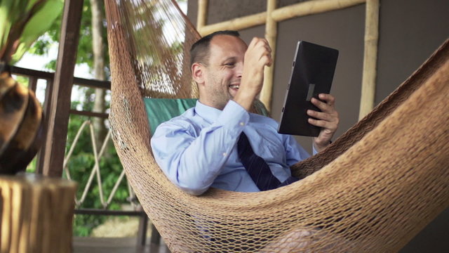 Successful businessman with tablet computer lying on hammock on terrace
