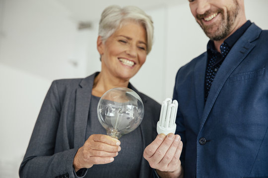 Businesswoman and businessman comparing regular and energy-saving lightbulb