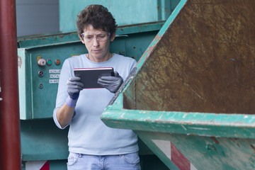 Woman at a waste container looking at digital tablet