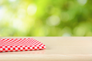 Red checkered cloth on wood table top in green bokeh abstract ba