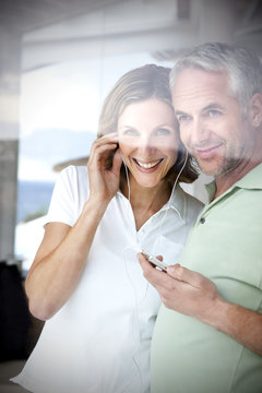 Portrait of smiling couple with earphones and mp3 player looking through window
