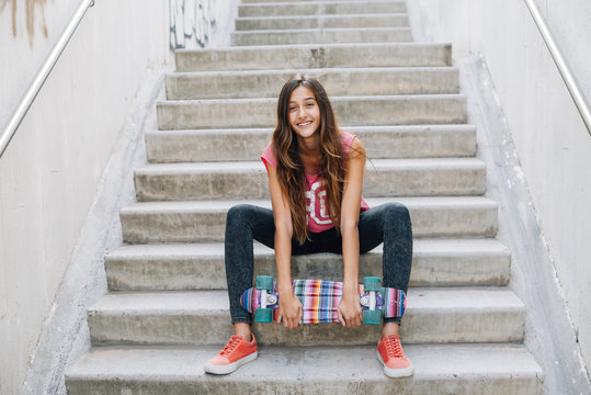 Portrait of happy teenage girl with colorful skateboard sitting on stairs