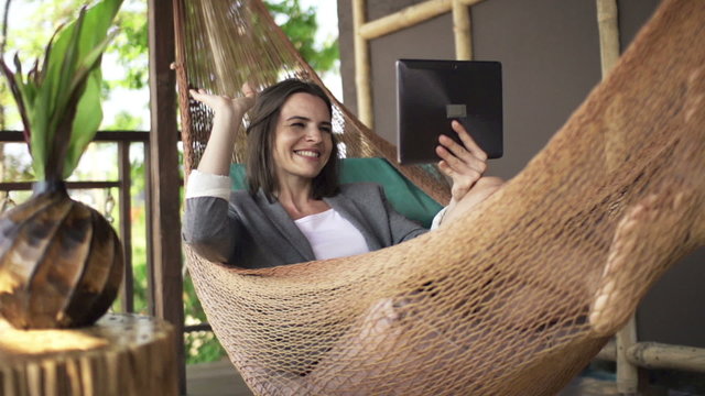 Businesswoman chatting on tablet lying on hammock, super slow motion 120fps
