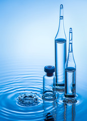 Medical ampoules and bottle on blue water background with splash