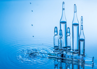 Medical ampoules and syringe on blue water background with splash