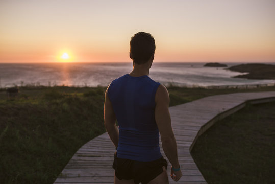 Spain, Ferrol, back view of a jogger standing on boardwalk watching sunset